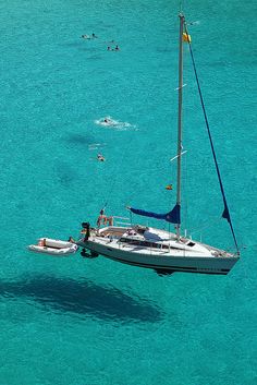 people swimming in the ocean next to a sailboat and a catamaran boat