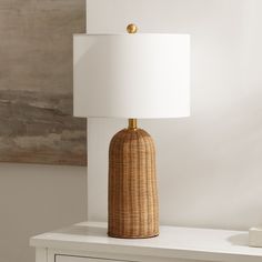 a wicker lamp sitting on top of a white table next to a dresser with drawers