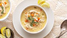 two bowls of chicken and dumpling soup on a table with lemons, spoons and napkin