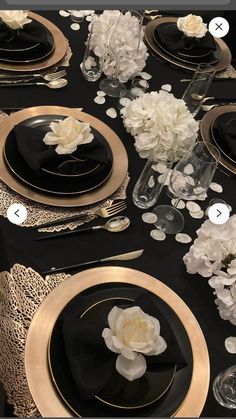 the table is set with black and gold plates, silverware, and white flowers