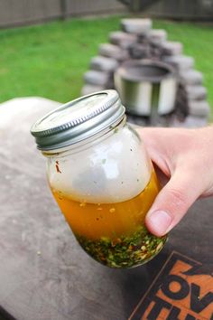 a person holding a jar filled with food on top of a wooden table in the grass