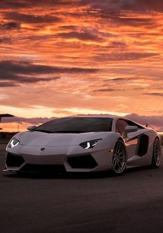 a white sports car parked in front of a red sky with clouds behind it at sunset