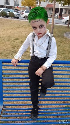 a young boy with green hair sitting on top of a blue bench wearing suspenders