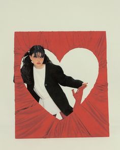 a woman in a black jacket and white shirt is standing behind a heart shaped photo