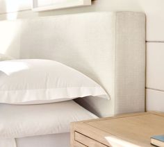 a bed with white pillows and a wooden night stand on the side table next to it