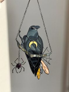 a stained glass bird hanging from a chain with two spider on it's side