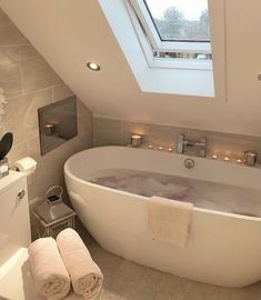 a bath tub sitting under a bathroom window next to a sink and toilet with two towels on it