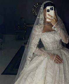 a woman in a wedding dress taking a selfie with her cell phone while wearing a veil