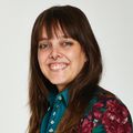 a woman with long brown hair and blue eyes smiles at the camera while wearing a floral shirt