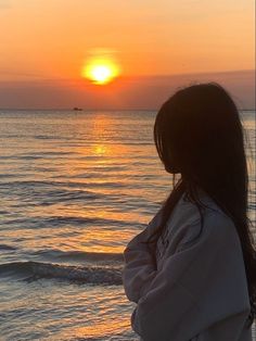 a woman standing on top of a beach next to the ocean at sun rise in the distance