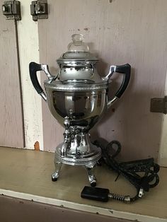 a silver tea pot sitting on top of a counter next to a phone charger