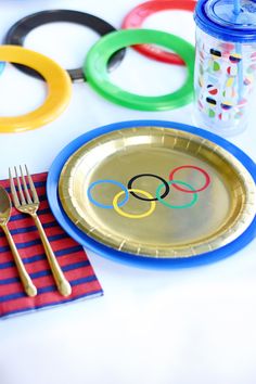 olympic themed plates and forks on a white table with colorful napkins, cups, and utensils