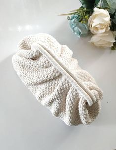 a white knitted bag sitting on top of a table next to a bouquet of flowers