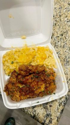 a plastic container filled with macaroni and cheese next to a chicken dish on top of a counter