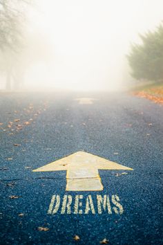 a road with an arrow painted on it and the words follow your dreams written in white