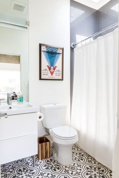 a white toilet sitting next to a sink in a bathroom under a framed poster on the wall