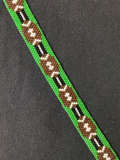 a green, brown and white beaded bracelet on a black background with an arrow