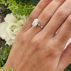 a woman's hand with a diamond ring on it and flowers in the background