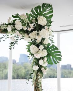 a cross decorated with white flowers and greenery in front of a window overlooking the water