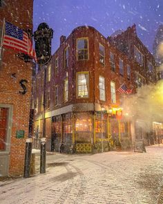 a snow covered street in front of a brick building with an american flag on it