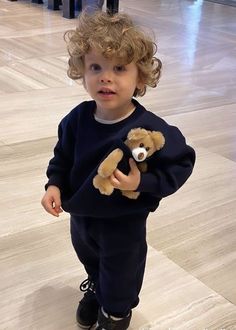 a little boy holding a teddy bear in his arms and wearing black shoes on the floor