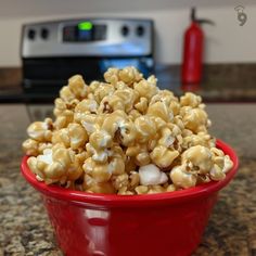 a red bowl filled with popcorn sitting on top of a counter next to an oven