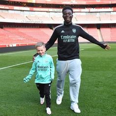 a man holding the hand of a young boy on a soccer field with an empty stadium in the background