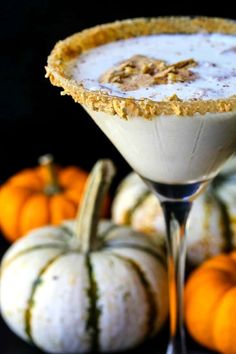 a drink in a martini glass next to mini pumpkins