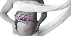 a pregnant woman with pink flowers painted on her belly and white scarf around her waist