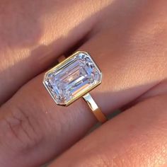 a woman's engagement ring with an emerald cut diamond in the center, on her finger