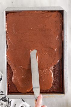 someone is spreading chocolate frosting on top of a brownie in a baking pan