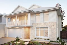 a white two story house with lots of windows and plants in the front yard area