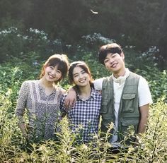 three people standing in tall grass smiling for the camera, with trees in the background