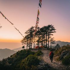 a person walking up a trail with flags flying in the air above them at sunset