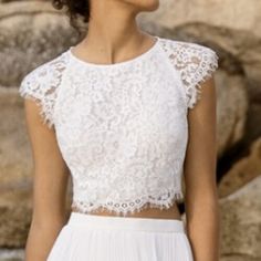 a woman wearing a white dress standing in front of some rocks and looking off into the distance