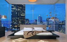 a large bed sitting in the middle of a bedroom next to a window with city lights on it