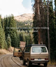 an suv driving down a dirt road next to a forest with a quote written on it