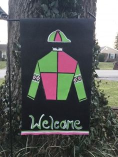 a welcome sign hanging from a tree in front of a house with green and pink clothing on it