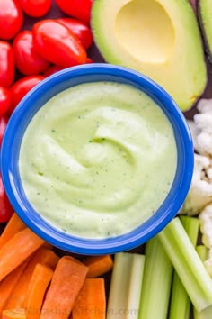 an avocado dip in a blue bowl surrounded by vegetables