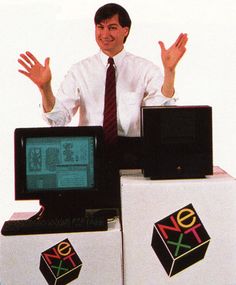 a man sitting on top of three computer monitors with their hands up in the air