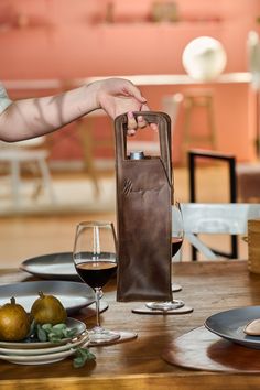 a person holding a wine bottle in front of a table with plates and glasses on it