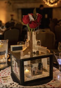 a table topped with a glass vase filled with flowers and pictures next to wine glasses