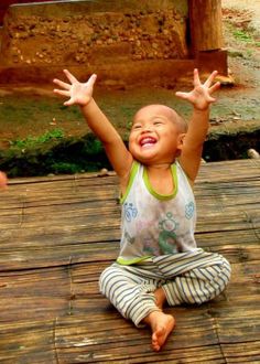 a little boy sitting on top of a wooden floor with his hands in the air