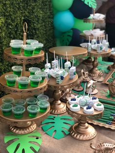 a table topped with lots of desserts covered in green and white frosted cupcakes