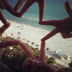 several fingers making a heart shape in front of the beach