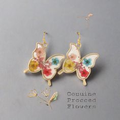 two butterfly shaped earrings with colorful flowers on them, sitting next to each other in front of a gray background