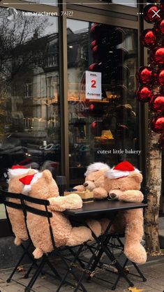 two teddy bears sitting at a table in front of a store window with santa hats on