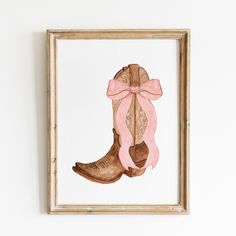 a painting of a cowboy boot with a pink ribbon tied around the bottom, mounted on a white wall