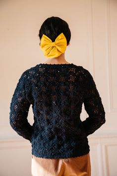 a woman with a yellow bow in her hair wearing a black sweater and tan pants