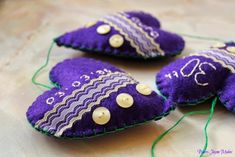 three purple hearts with white buttons and green thread on a tablecloth covered cloth surface